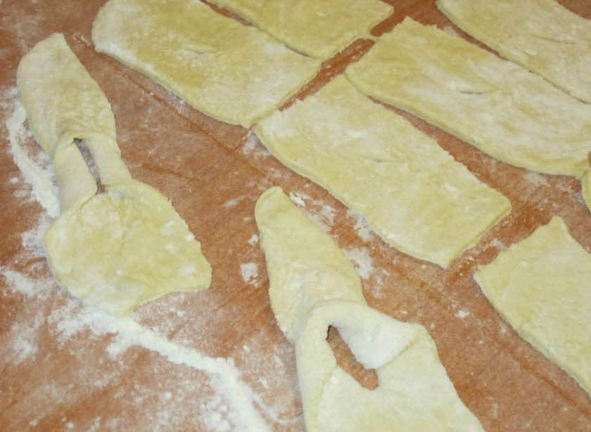 1. Этап. Пышный хворост на кефире: 1. Очень простое тесто на кефире: сразу добавляем в кефир соду, ждем, пока она погасится, после чего добавляем все остальные ингредиенты. Замешиваем эластичное тесто, разделяем его на части. Затем каждую часть нужно раскатать и вырезать прямоугольные полоски (примерно 2,5*7см). В центре каждого из них сделайте небольшой надрез, через который вывернуть одну часть наружу.