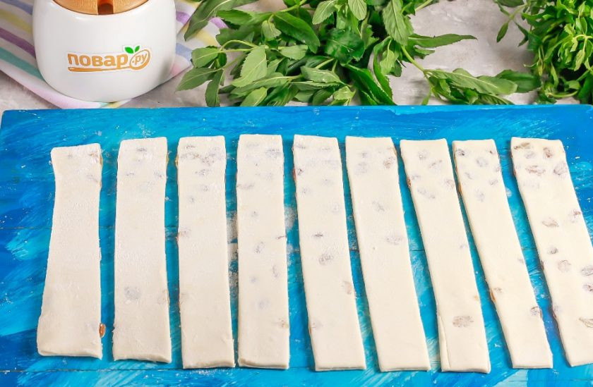 1. Этап. Слоеные палочки с изюмом и сахаром: Раскатайте второй пласт теста в такой же прямоугольник и накройте им начинку сверху. Пройдитесь скалкой, впечатывая сахар и изюм в тесто. Нарежьте тесто длинными полосами по 1,5-2 см. шириной. Смажьте яичным желтком или молоком.
