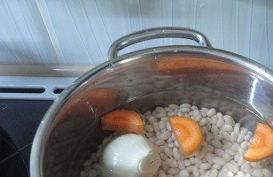 1. Этап. Пюре из белой фасоли по-румынски: Замочите фасоль на 8-10 часов. Желательно за это время несколько раз воду поменять. Для варки залейте фасоль свежей водой в соотношении 1:5. Добавьте крупно нарезанную морковь и одну очищенную целую луковицу. Доведите до кипения, убавьте нагрев и варите 1,5 часа. Солить можно только в самом конце варки. Но обратите внимание, в этом рецепте мы будем добавлять чеснок, растертый с солью. За 5 минут до готовности фасоли добавьте лавровый лист.