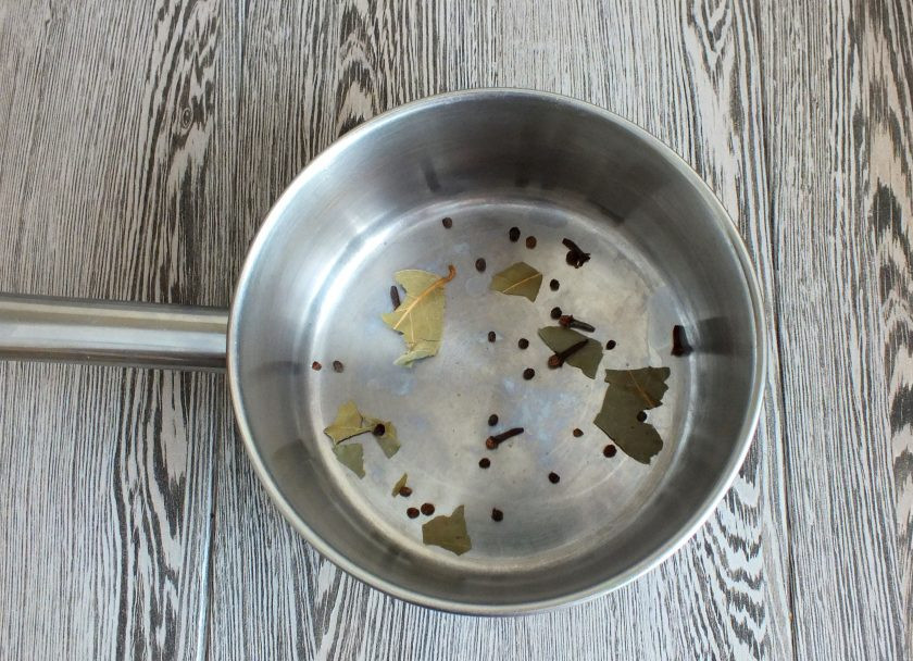 1. Этап. Домашние шпроты из кильки: Возьмите сотейник или кастрюлю с толстым дном. На дно раскрошите 1 лавровый лист, положите половину указанного количества перца и гвоздики.