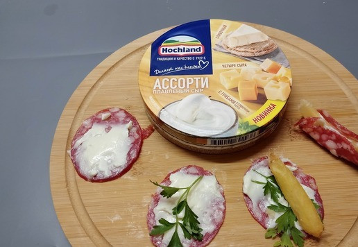 1. Этап. Мини-бутерброды Ассорти: Ломтик сырокопченой кобасы намазать плавленым сыром. Выложить листик петрушки. В середину выложить ломтик картофеля фри. Соединить края.