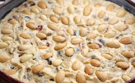 1. Этап. Рождественский кекс с сухофруктами и орехами: Смажьте форму для выпечки сливочным маслом и немного присыпьте мукой. Влейте тесто, разровняйте и украсьте очищенным миндалём.