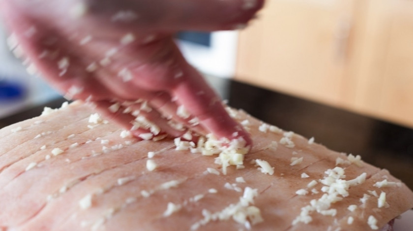 1. Этап. Свинина запеченная с чесноком: Спустя полчаса нашпигуйте свинину мелко нарезанным чесноком. Особенно интенсивно нарезанный чеснок нужно вставлять в надрезы, но и просто по поверхности распределить нужно. Чеснока не жалейте, его должно быть много.