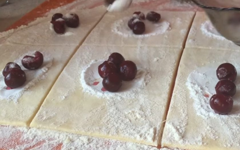 1. Этап. Слоеные пирожки с вишней на пиве: 3. Раскатайте тесто в большой не очень тонкий пласт. Поделите пласт на квадратики. На каждый выложите половину чайной ложки крахмала, вишни и присыпьте половиной чайной ложки сахара. Залепите пирожки в форме квадратиков или треугольников.