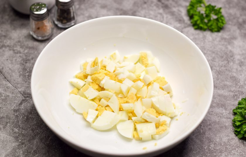 1. Этап. Салат Фантазия с яйцами и сыром: Куриные яйца отварите 10 минут и остудите, почистите. Нарежьте яйца небольшими кубиками. Переложите яйца в салат.