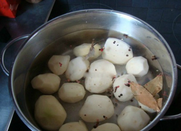 1. Этап. Картофель, запеченный с мясом и грибами: 1. Картофель хорошо промойте под проточной водой, очистите от кожуры. В кастрюлю налейте воды, поставьте на средний огонь и положите в неё картошку. Добавьте лавровый лист и душистый перец горошком. Варите примерно 15 минут после закипания воды.