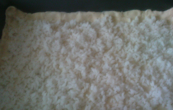 1. Этап. Рыбный пирог из сайры: Противень застилаем бумагой для выпечки (или просто смазываем маслом). Раскатываем один лист теста в пласт, выкладываем по форме противня. Сверху распределяем отварной рис.