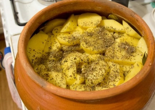 1. Этап. Оленина в горшочке: Добавьте в горшочек к мясу толченые кедровые орешки. Затем очистите картофель, вымойте его и нарежьте на кружочки. Выложите картофель поверх мяса с овощами, посолите, поперчите и добавьте сушеный базилик.