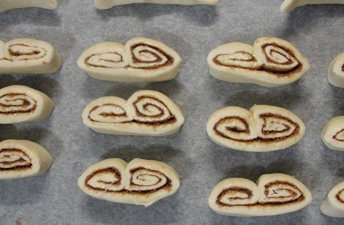 1. Этап. Ушки из теста: Извлекаем тесто из холодильника и нарезаем его острым ножом на печеньки. Раскладываем их на противень, застеленный бумагой для выпечки.