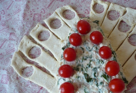 1. Этап. Рождественская елка из слоеного теста: Удалите излишки теста, сделайте круги на каждой пластинке по бокам смеси, используя крышку от бутылки. Поверх начинки положите помидоры черри (как на фото).