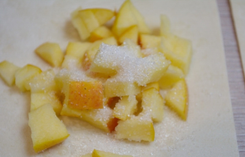 1. Этап. Конвертики из слоеного бездрожжевого теста: Сверху на яблоки выложите чайную ложку сахара. При запекании сахар соединится с яблочным соком и образуется карамель.