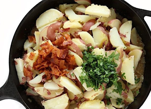 1. Этап. Деревенский картофельный салат: 5. Немного остывший картофель разрежьте на небольшие кусочки и добавьте к луку. Помойте и измельчите зелень, добавьте в сковороду к луку, а также зелень и бекон.