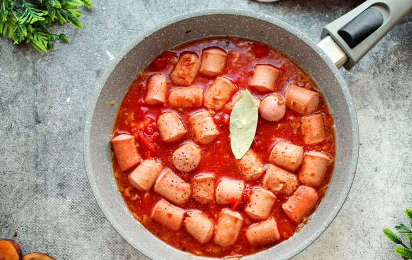 1. Этап. Сосиски в томатном соусе с рисом: Влейте в сковороду горячую воду, добавьте лавровый лист, посолите, поперчите и перемешайте.