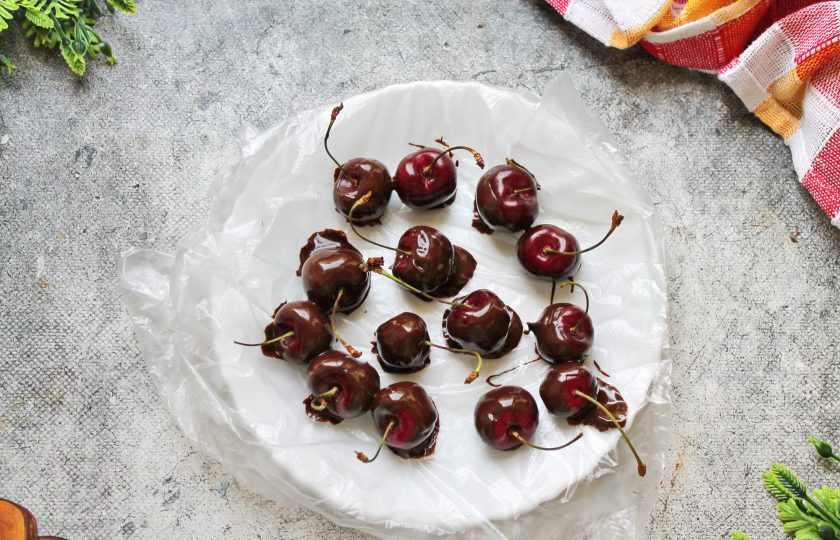 1. Этап. Летний торт: Каждую черешенку возьмите за хвостик и опустите в шоколад почти до конца. Достаньте, дайте стечь лишнему шоколаду и выложите на тарелку. Уберите в сторону, чтобы шоколад застыл.