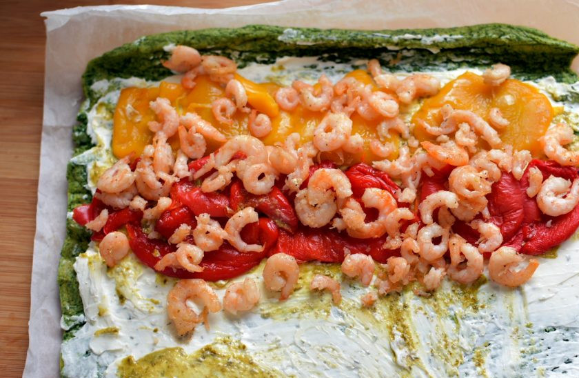 1. Этап. Зеленый рулет с креветками и болгарским перцем: Остывший рулет аккуратно развернуть, смазать творожным сыром и поверх него немного песто. Разложить кусочки перца, чередуя их по цвету. Сверху выложить креветки.