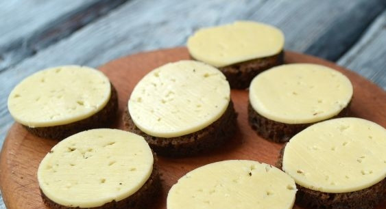 1. Этап. Канапе для праздничного стола: Оставшиеся кусочки чёрного хлеба сделайте круглыми. На них уложите сыр (его тоже нарежьте кружочками).