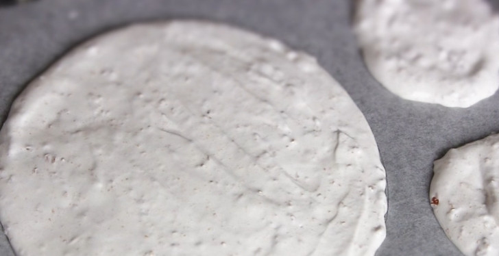 1. Этап. Торт-безе с масляным кремом: 5. Нарисуйте на пергаменте 2 круга диаметром 25 см, аккуратно распределите белковую массу для 2 коржей. Рядом сделайте 2 небольшие лепешки, которые пойдут на крошку для украшения торта.