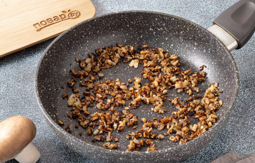 1. Этап. Шампиньоны со сливочным сыром: Разогрейте сковороду с растительным маслом на среднем огне и обжарьте репчатый лук с ножками шампиньонов до золотистого цвета. Посолите и поперчите в конце по вкусу.