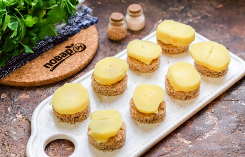 1. Этап. Канапе с килькой и яйцом: Картофель отварите заранее и нарежьте небольшими кружочками, выложите на сливочное масло.