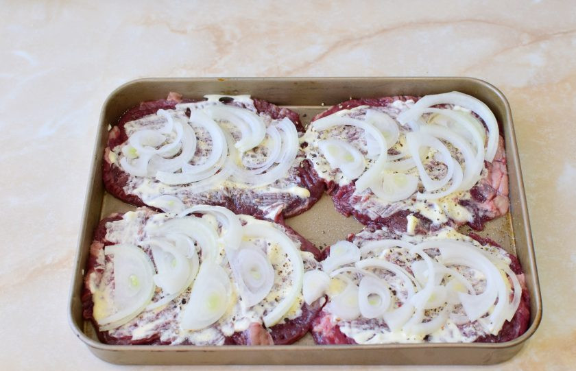 1. Этап. Телятина в духовке с ананасами: Лук очистите и нарежьте полукольцами. Разложите нарезанный лук по мясу.