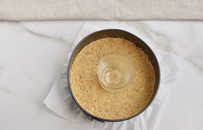 1. Этап. Торт из творога: Разъемную форму проложите пергаментной бумагой. Выложите массу из печенья и хорошо утрамбуйте ее донышком стакана, формируя плотный корж. Охладите в холодильнике минут 15.