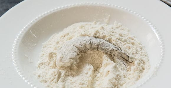 1. Этап. Креветки в кокосовой стружке: Приготовьте 3 тарелки. В одну всыпьте муку. Во второй взбейте яйца. В третью положите кокосовую стружку. Посыпьте креветки мукой.