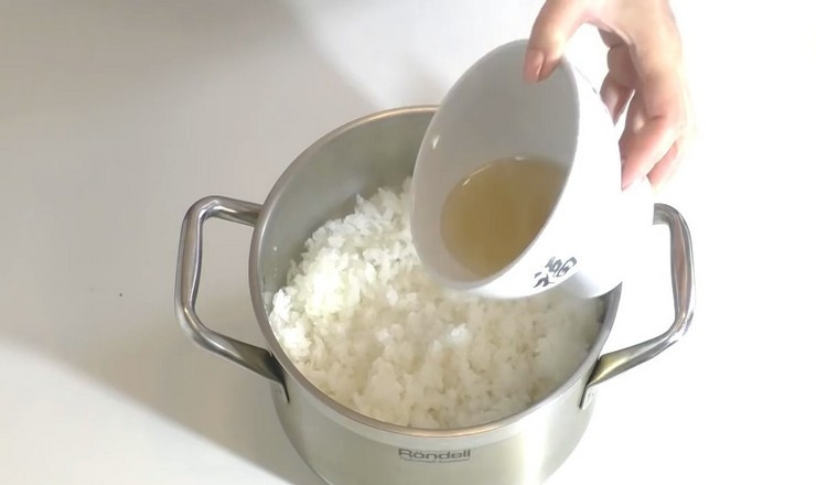 1. Этап. Роллы в духовке: Готовый рис выложите в посуду побольше, слегка разрыхлите легкими движениями при помощи деревянной лопатки, влейте заправку и аккуратно перемешайте рис.