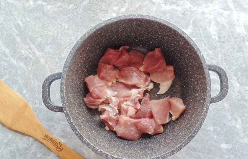 1. Этап. Мясо с капустой и яблоками: Свинину вымойте, нарежьте небольшими кусочками. Переложите в казан или сотейник. Добавьте подсолнечное масло.