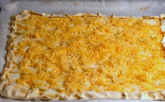 1. Этап. Выпечка из слоеного теста в духовке: 4. Вымойте, обсушите, очистите от кожуры и нарежьте небольшими ломтиками грушу. Разложите её ровным слоем на тесто. Натрите на мелкой или средней терке сыр, присыпьте сверху. При желании такую выпечку из слоеного теста в духовке в домашних условиях можно дополнить ароматными травами: розмарином или тимьяном, например.