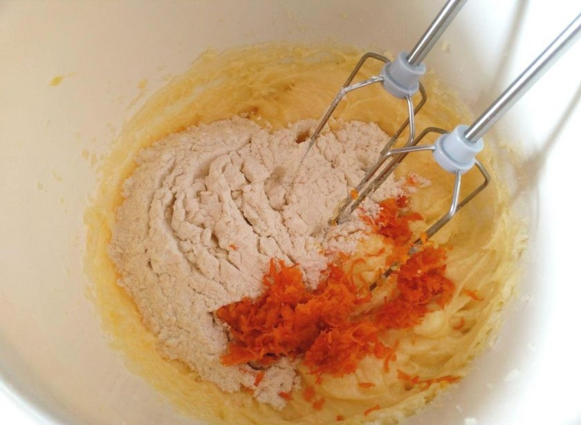 1. Этап. Пирожные Ламингтон, ароматизированные цедрой апельсина: Добавьте цедру апельсина (снятую с плода при помощи мелкой тёрки), всыпьте муку, просеянную и смешанную с разрыхлителем.