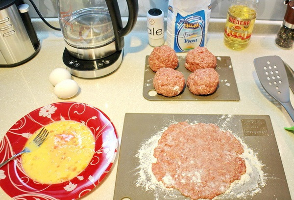 1. Этап. Бризоль в духовке: Далее мы разделяем наш фарш на несколько одинаковых шариков, из этого количества фарша их должно получиться 5-6. Теперь посыпаем стол мукой, выкладываем на него один мясной шарик и раскатываем его или расплющиваем в лепешку, в плоской тарелке взбиваем одно яйцо.