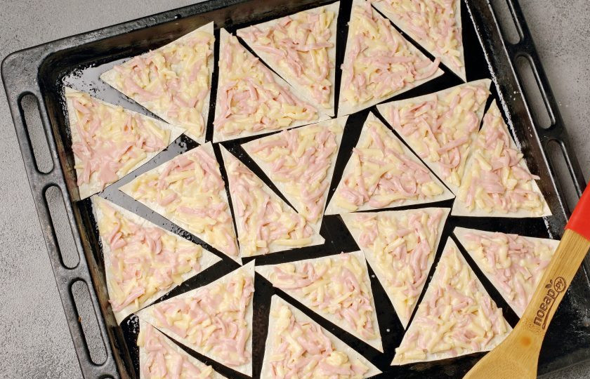 1. Этап. Чипсы из лаваша с яйцом, сыром и колбасой: Нарезанный лаваш выложите на противень и смажьте начинкой. Запекайте в духовке при температуре 180 градусов около 15 минут. Время зависит от желаемой готовности чипсов, кто-то любит помягче, а кто-то предпочитает именно похрустеть.