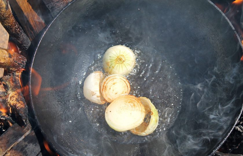 1. Этап. Креветки в казане на костре: Установите подставку под казан и разведите под ним костер. В казан налейте растительное масло и разогрейте. Добавьте очищенный репчатый лук, если он крупный разрежьте пополам, и обжарьте мешая, до золотистого цвета. Удалите его из казана.