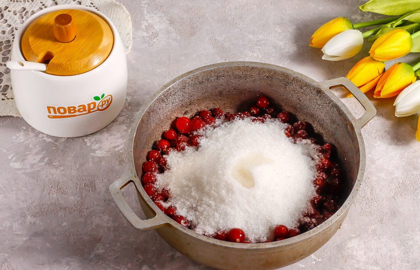 1. Этап. Варенье из клюквы с грецкими орехами: Пересыпьте ягоды в казан или кастрюлю с антипригарным дном. Всыпьте туда же сахарный песок и влейте лимонный сок. Если клюква слишком кислая, то можно обойтись и без него.