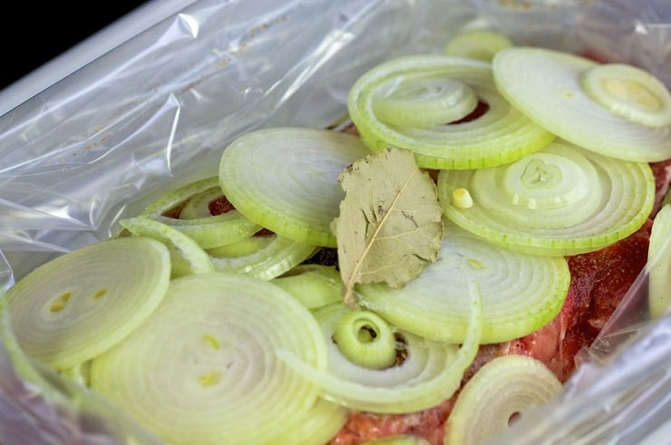 1. Этап. Ростбиф из говядины классический: На говядине распределите колечки второго лука, лавровый лист и перец горошком. Заверните пакет, оставьте мясо на 5 часов мариноваться в холодильнике.