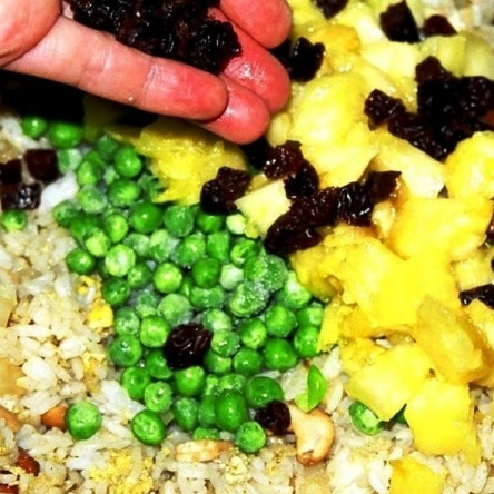 1. Этап. Рис с ананасом: Ананас разрезаем вдоль пополам, из обеих половинок аккуратно вырезаем мякоть. Мякоть нарезаем небольшими кубиками, а оставшуюся лодочку из ананаса не выбрасываем - в ней будем эффектно подавать блюдо. Добавляем в сковороду мякоть ананаса, замороженный горошек (по желанию) и изюм (по желанию).