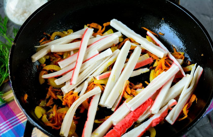 1. Этап. Салат с жареными крабовыми палочками: К размягченному луку и морковке добавьте крабовые палочки.