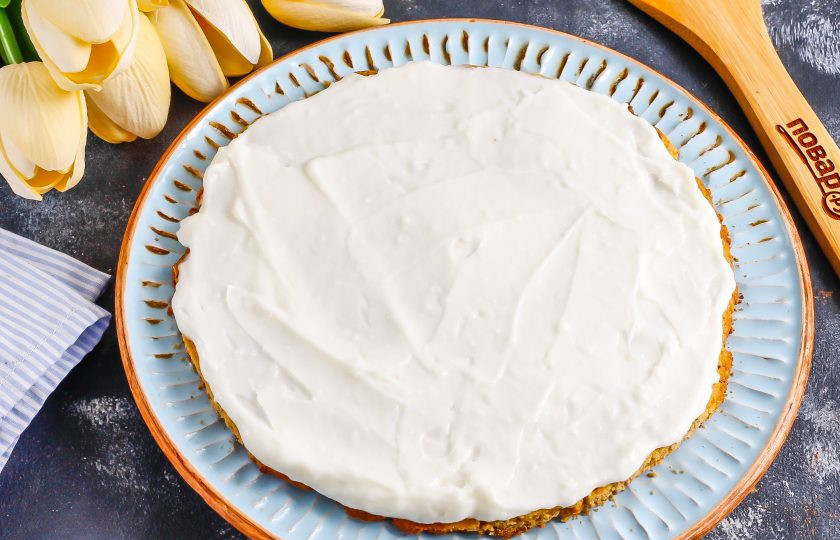 1. Этап. Песочный торт с орехами: Остывший корж выложите на тарелку и смажьте сметанным кремом. По желанию корж сначала можно пропитать сиропом или топингом.