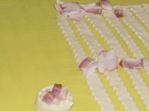 1. Этап. Булочки-улитки с беконом: По ломтику бекона уложите в начале полосок и в середине, а потом скрутите тесто с беконом в спираль.