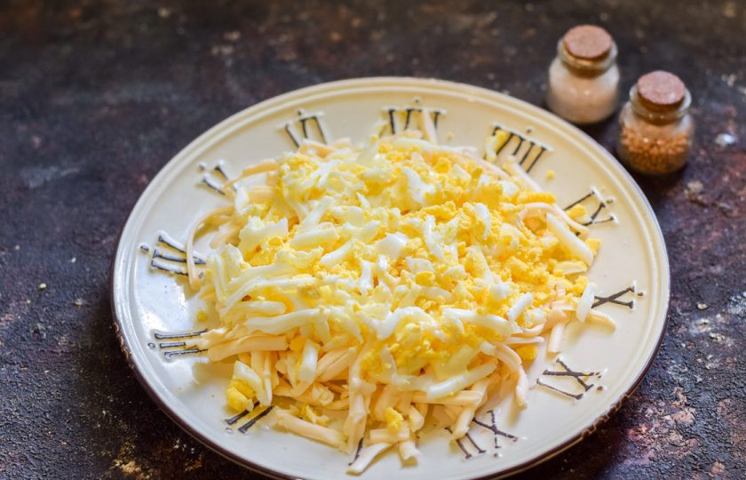 1. Этап. Крабовый салат Новинка с сухариками: Куриное яйцо отварите и натрите на средней терке, выложите поверх сыра — это будет второй слой салата. Далее смазывайте каждый слой небольшим количеством майонеза.