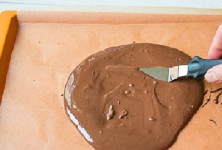 1. Этап. Сникерс в домашних условиях: Растопим на водяной бане половину шоколада и выльем его в форму, застеленную пергаментом. Разравниваем пласт лопаткой и ставим в морозилку.