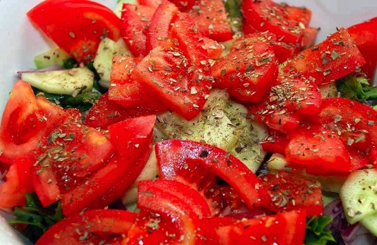 1. Этап. Вкусный салат из кальмара: Помидоры выбирайте мягкие и сочные. Их хорошо вымойте, высушите и нарежьте крупными дольками. Сок, выделившийся при нарезке, вылейте в салат, а сами дольки уложите поверх огурца с луком. Посыпьте всё сухим орегано, по вкусу поперчите и посолите.