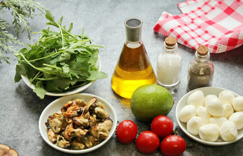 1. Этап. Салат с мидиями, моцареллой и рукколой: Подготовьте все необходимые ингредиенты для приготовления салата с мидиями, моцареллой и рукколой. Мидии откиньте на сито и дайте полностью стечь маслу или жидкости. Черри и рукколу сполосните и обсушите.