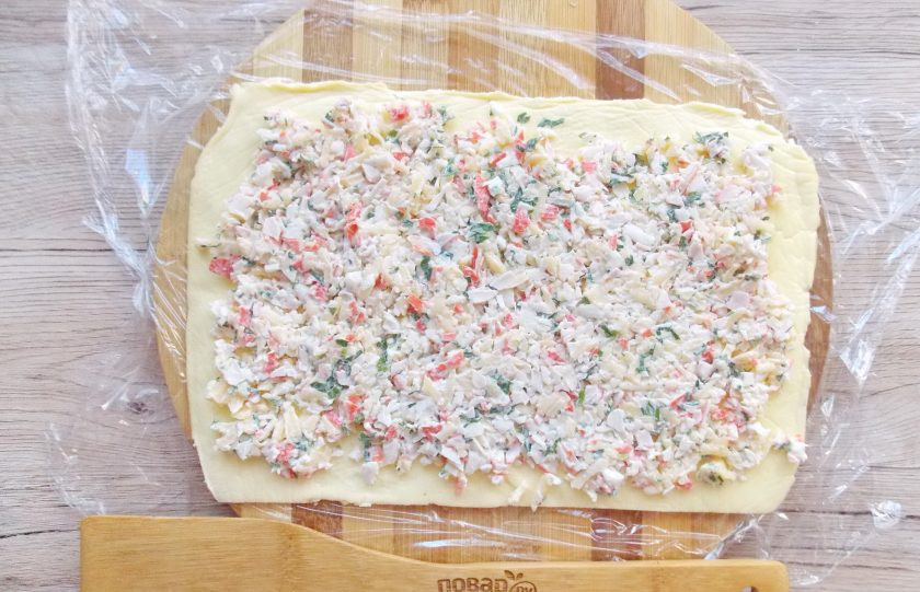 1. Этап. Яичные рулетики из крабовых палочек с сыром: Дайте омлету остыть. Очень аккуратно, чтобы не повредить омлет, отделите его от пергамента. Выложите его на пищевую пленку и распределите начинку.