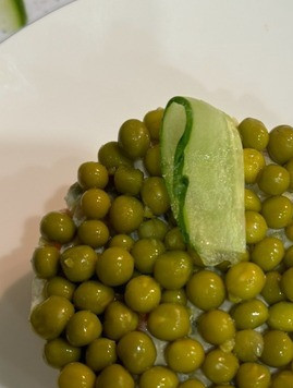 1. Этап. Рождественский салат Оливье: С порционного салата снимаем кольцо. Сверху выкладываем тонким слоем зеленый горошек и слайсы свежего огурца, формируя бантик