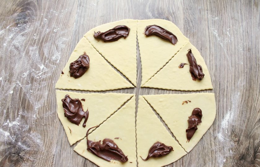 1. Этап. Рогалики с нутеллой: На широкий край треугольников выложите шоколадную пасту. Сверните рогалики от широкого края к узкому. Защипните края, чтобы паста не вытекла.