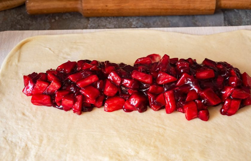 1. Этап. Штрудель с яблоками и вишней: На край теста выложите яблочно-вишневую начинку, как на фото.