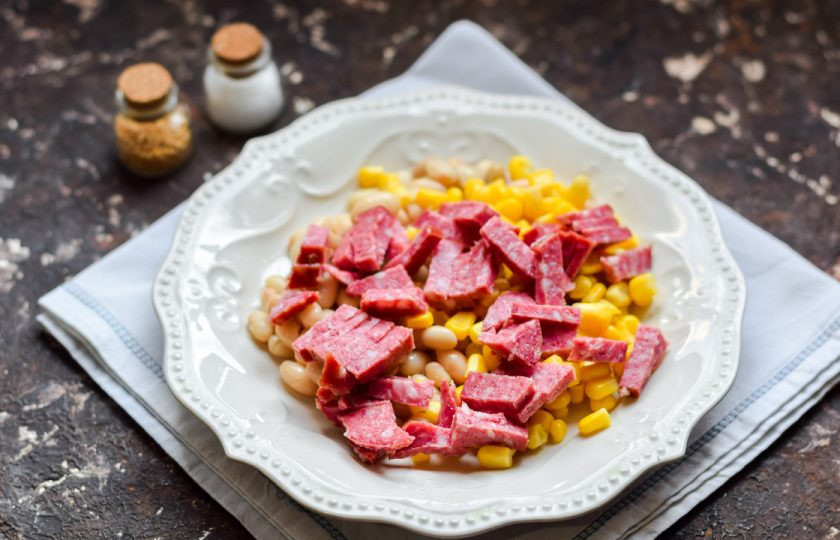 1. Этап. Салат с кукурузой, колбасой и фасолью: Копченую колбасу нарежьте небольшими кусочками и переложите в салат.