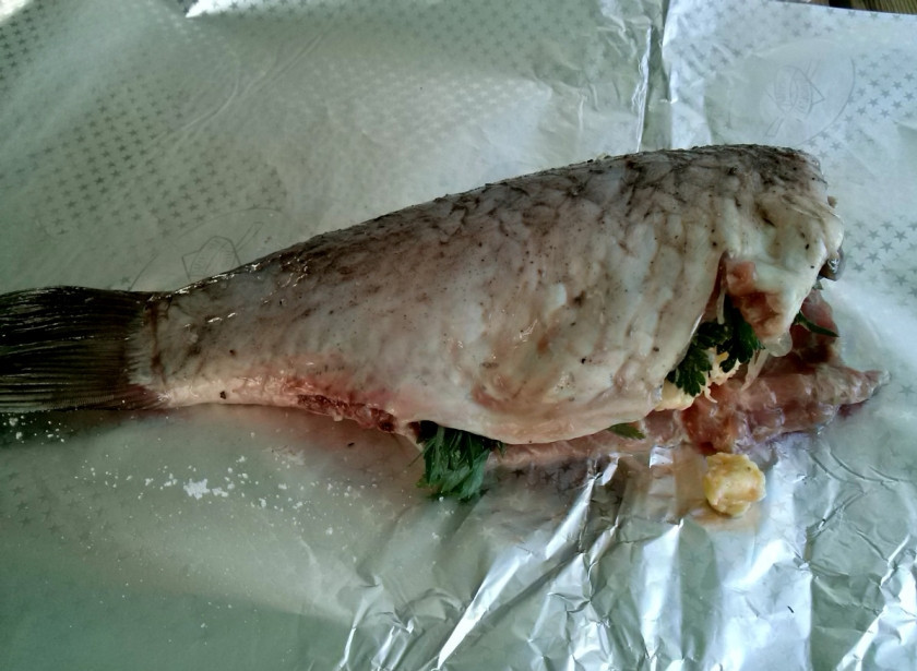 1. Этап. Сазан в фольге в духовке: Положите тушку сазана на фольгу. Внутрь рыбы добавьте веточки зелени и нарезанный ломтиками корень имбиря. Добавьте сливочное масло.