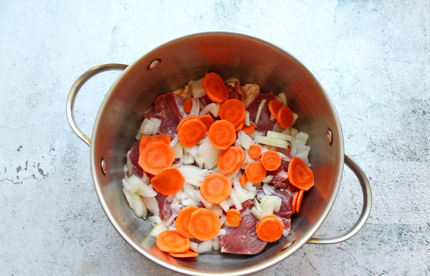 1. Этап. Хашлама из говядины на пиве: Репчатый лук почистите и порежьте, морковь почистите, сполосните и порежьте колечками. Выложите овощи к мясу.